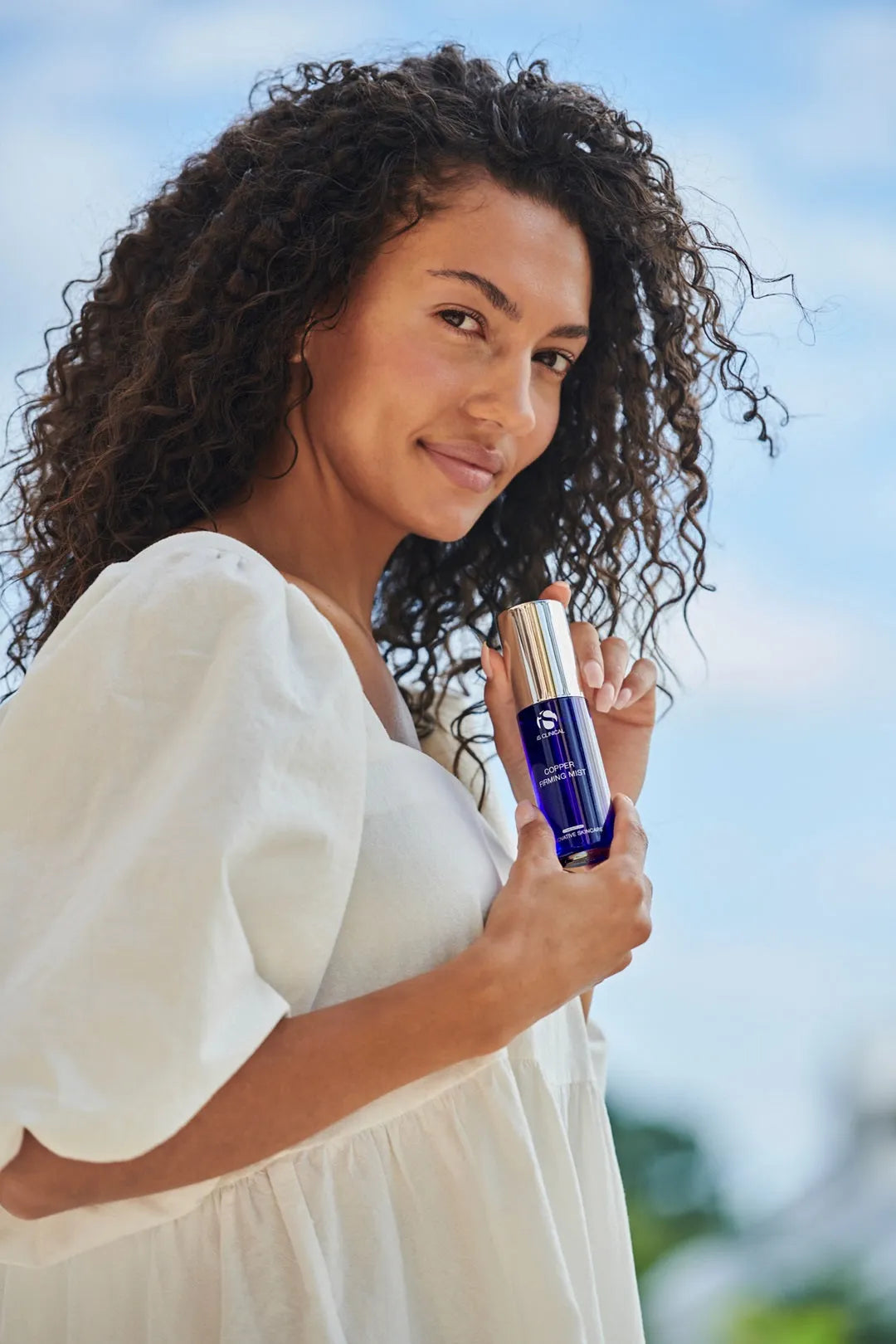 Woman holding a skincare product with a blurred natural background