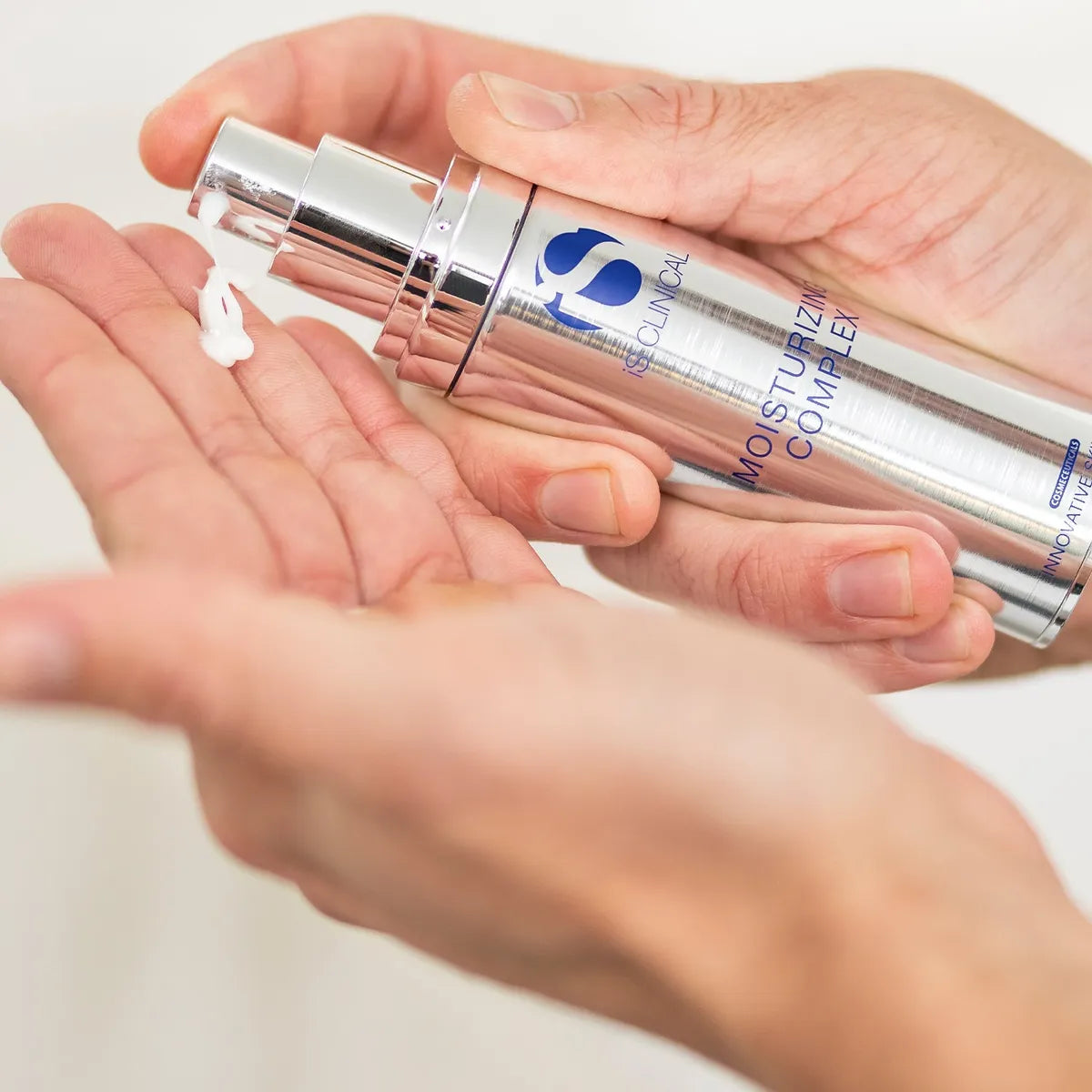 Hand holding a silver skincare bottle labeled 'iS Clinical' on a light background