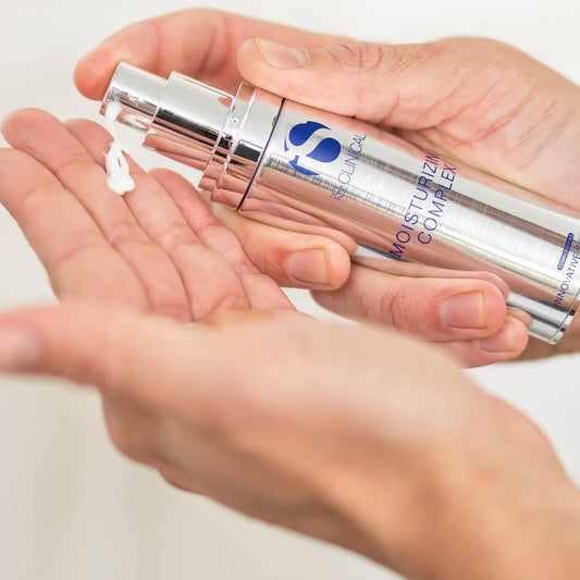 Hand holding a silver skincare bottle labeled 'iS Clinical' on a light background