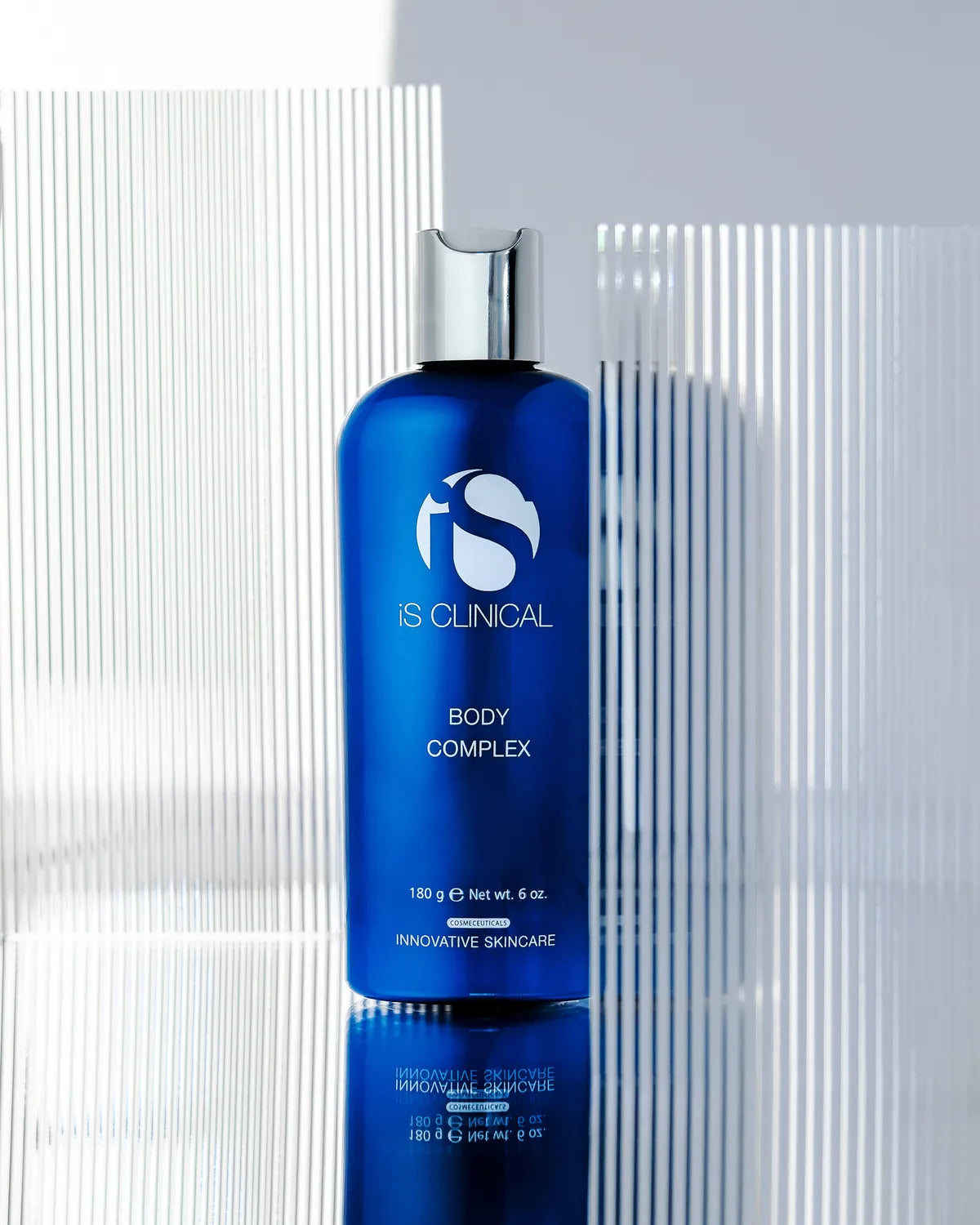 Blue bottle of IS Clinical Body Complex on a reflective surface with a white background