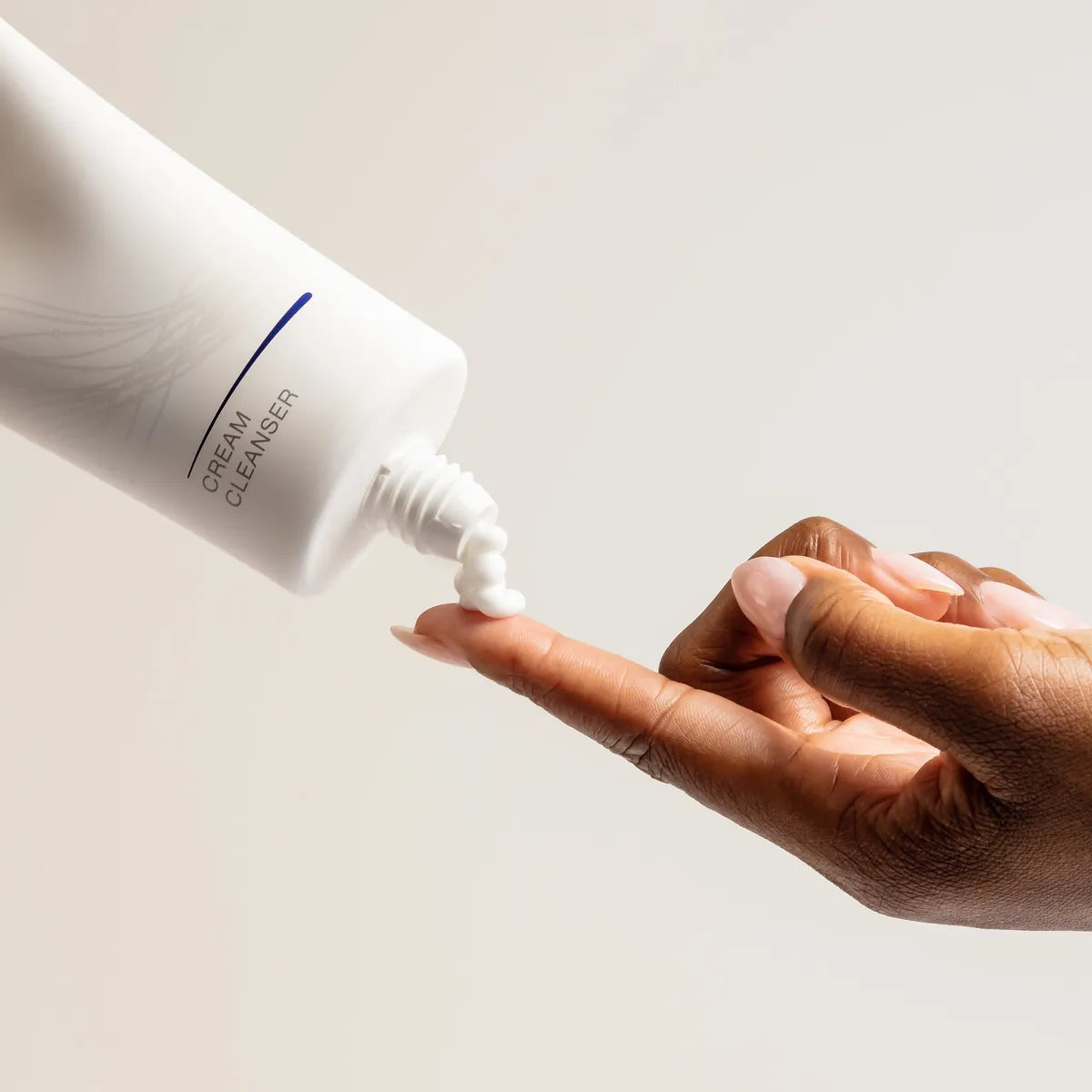 Hand applying cream cleanser from a bottle on a neutral background