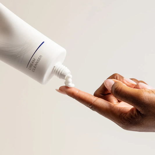 Hand applying cream cleanser from a bottle on a neutral background